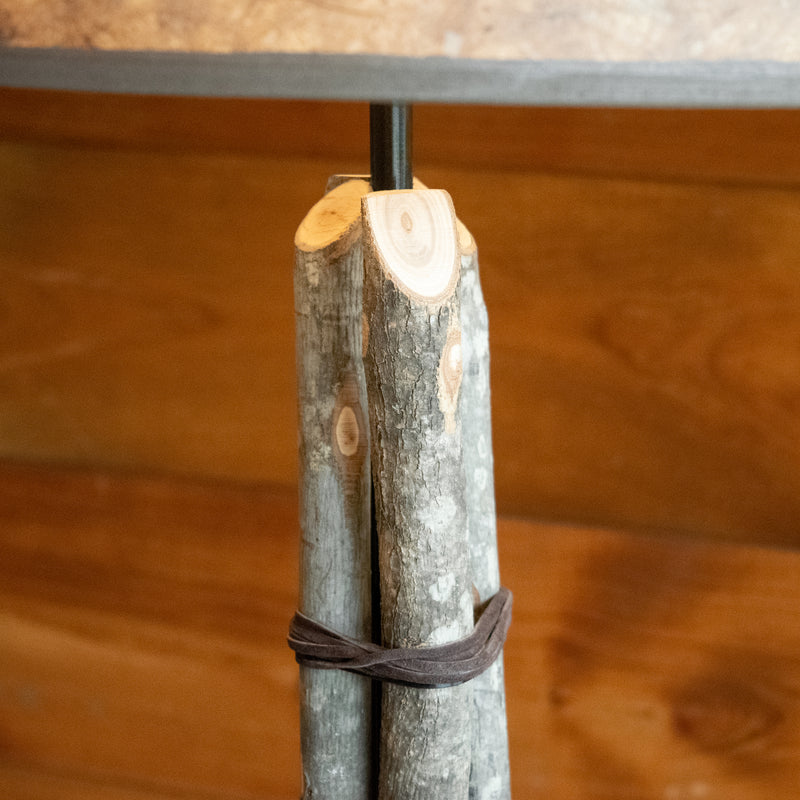 Close-up of the column of a rustic bundled wood floor lamp against a rustic wooden wall