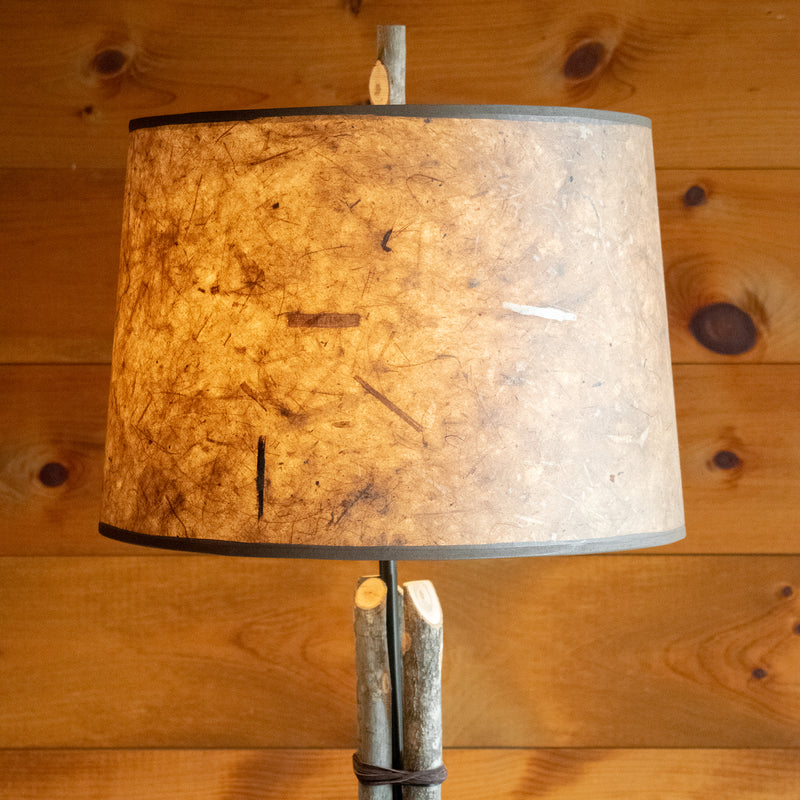Close-up of the lampshade on a rustic bundled wood floor lamp on a wide-plank wood floor against a rustic wooden wall 