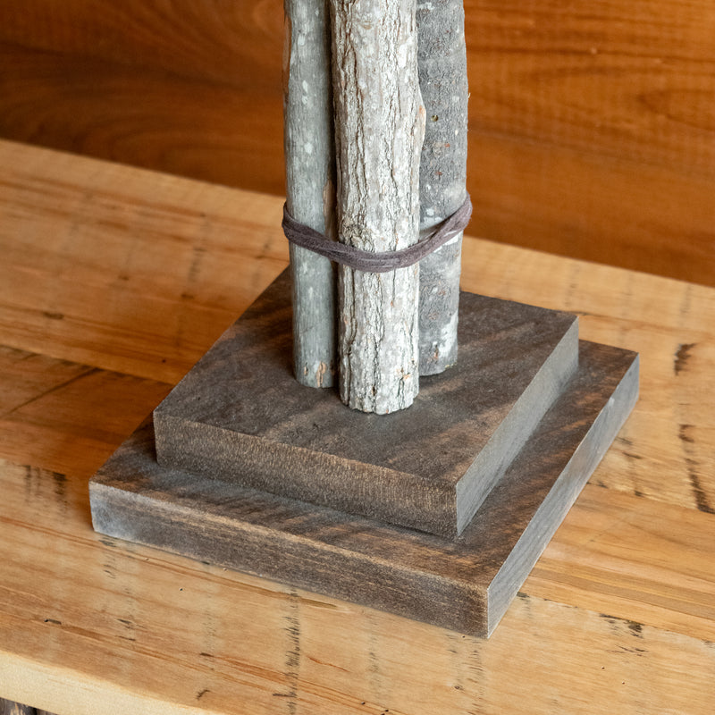 Close-up of the base of a rustic bundled wood tall table lamp on a wooden table against a rustic wooden wall