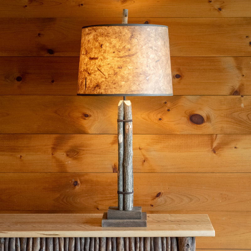 Front view of a rustic bundled wood tall table lamp on a wooden table against a rustic wooden wall