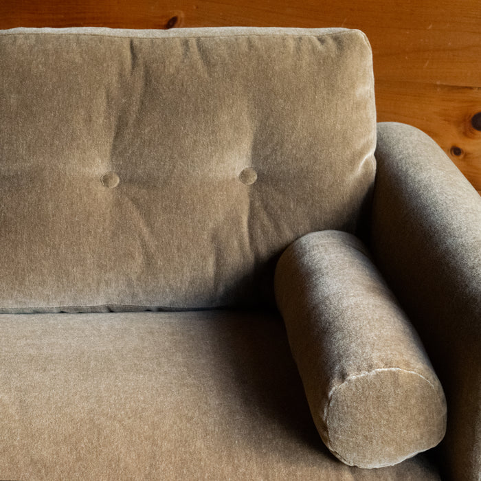 Close-up of the back cushion and bolster pillow of a rolled arm sofa upholstered in neutral mohair against a rustic wooden wall