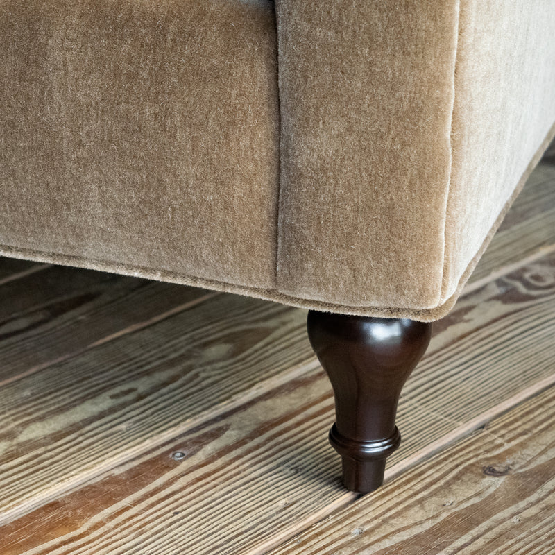 Close-up of the leg of a rolled arm sofa upholstered in neutral mohair on a wide-plank wood floor