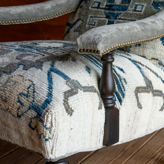 The arm close-up of a lounge chair upholstered in a cream, blue, and sage green vintage rug-inspired fabric