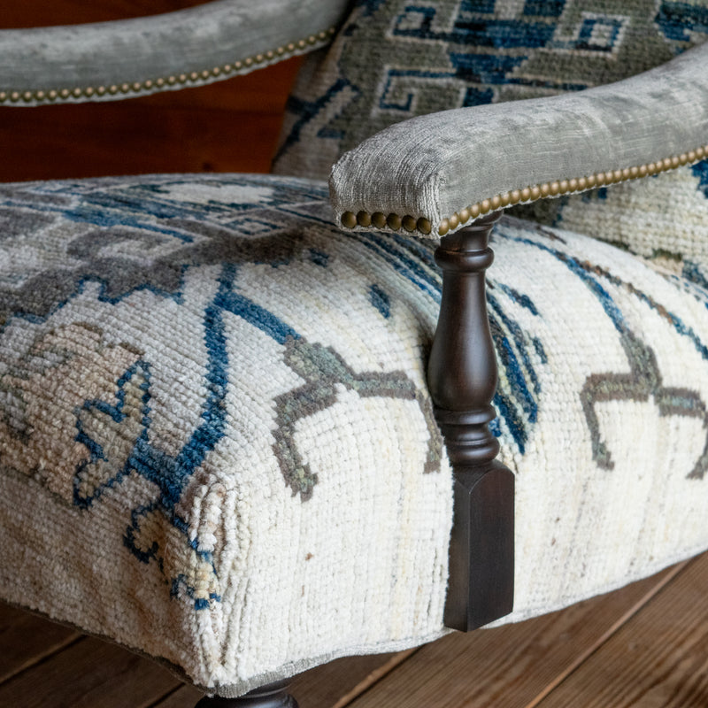The arm close-up of a lounge chair upholstered in a cream, blue, and sage green vintage rug-inspired fabric