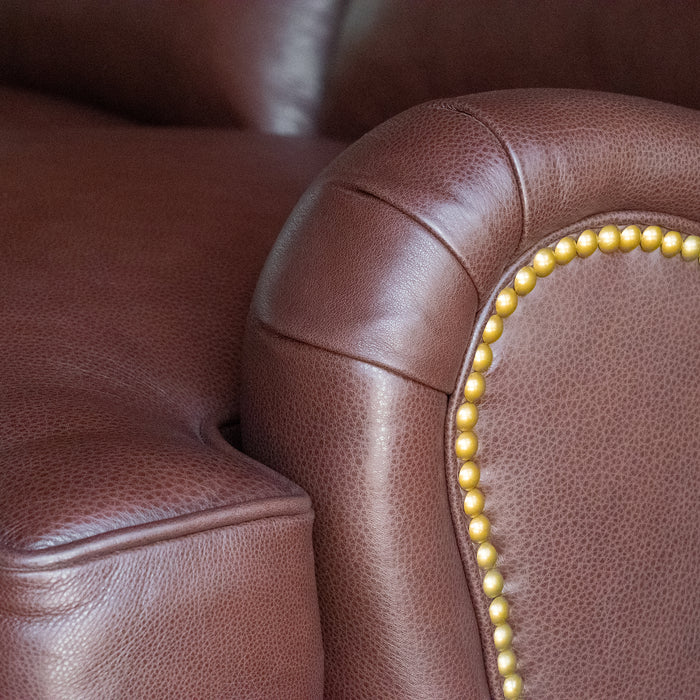 Arm close-up of a dark brown leather three-seat sofa with nailhead trim