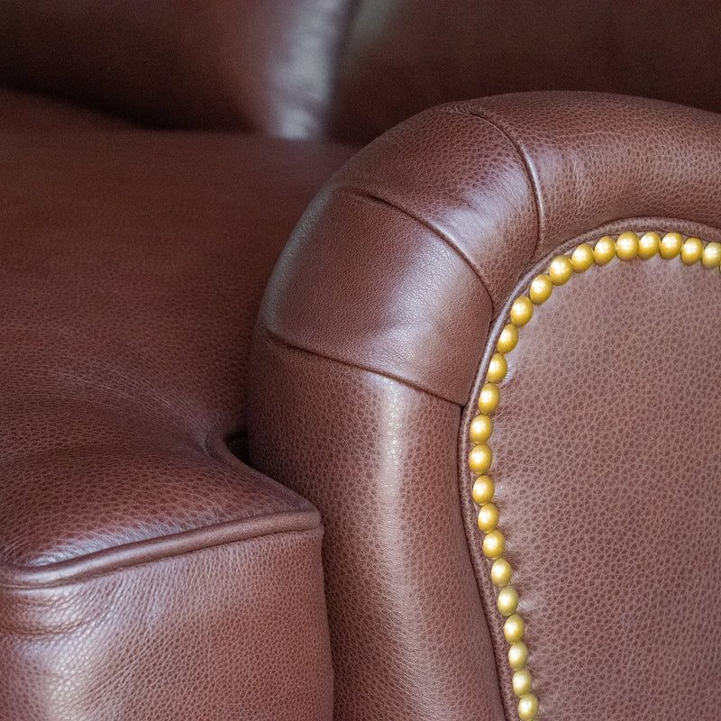 Arm close-up of a dark brown leather three-seat sofa with nailhead trim
