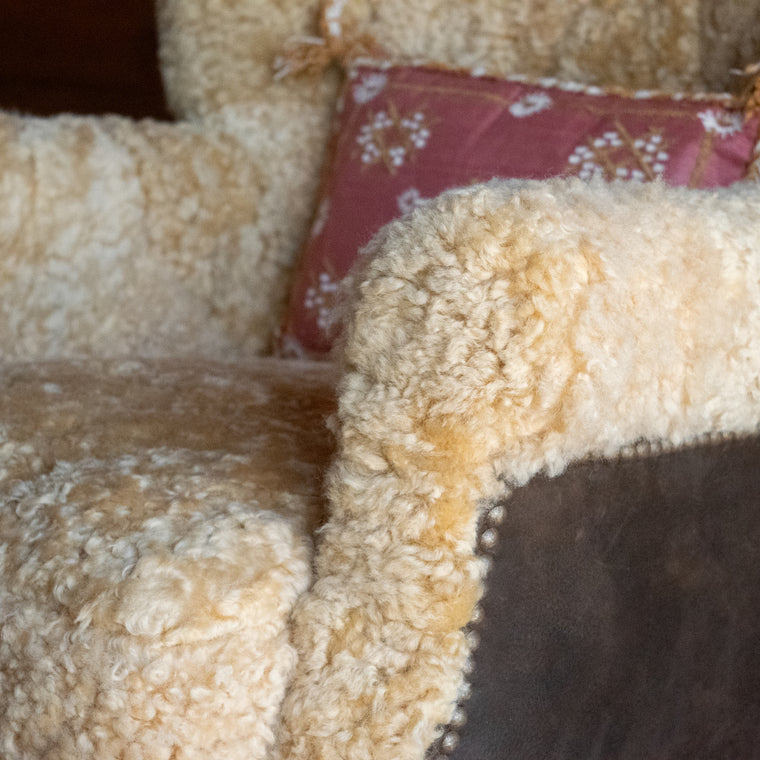 Angled back view of a golden shearling chair with contrasting brown suede leather back and sides against a wooden wall