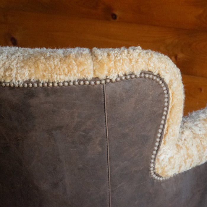 Close-up of the back of a golden shearling chair with contrasting brown suede leather back and sides against a wooden wall