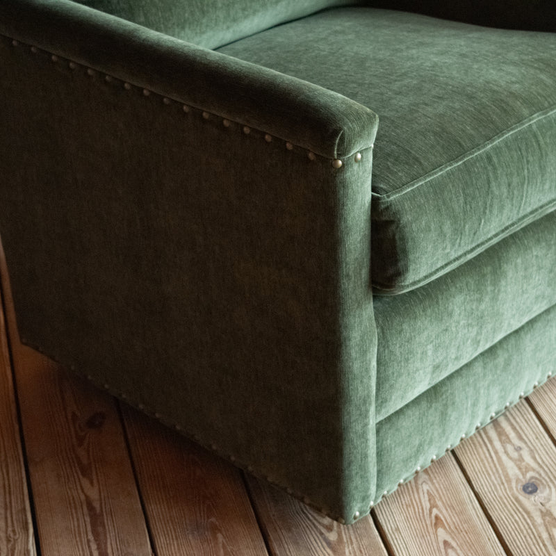 Close-up of the arm of a swivel chair with track arms upholstered in a green velvet-chenille fabric on a wooden floor