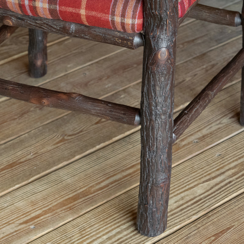 Close-up of the hickory frame of a chair upholstered in a rustic red plaid fabric on a wide-plank wood floor