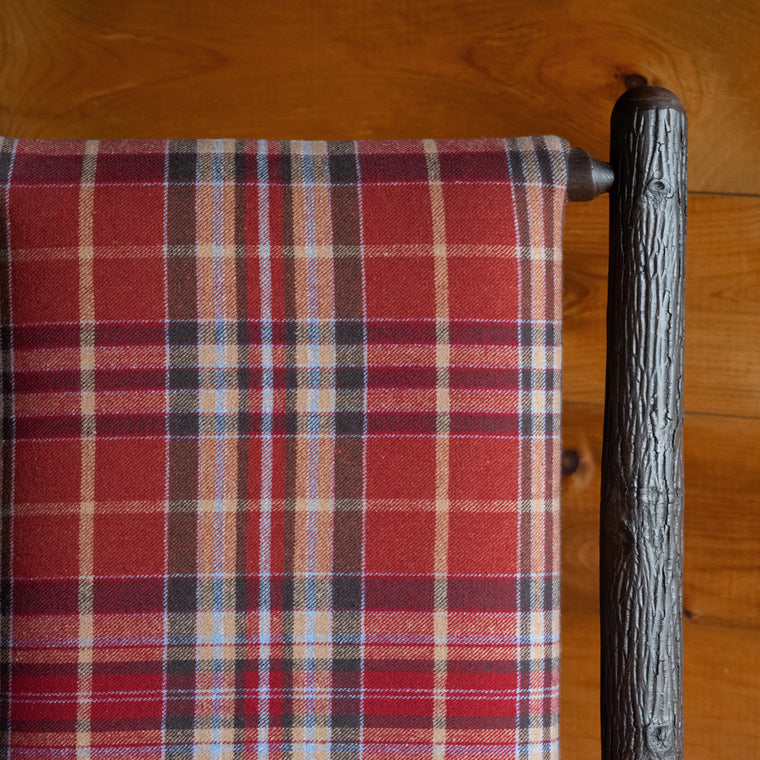 Close-up of the hickory frame of a chair upholstered in a rustic red plaid fabric on a wide-plank wood floor