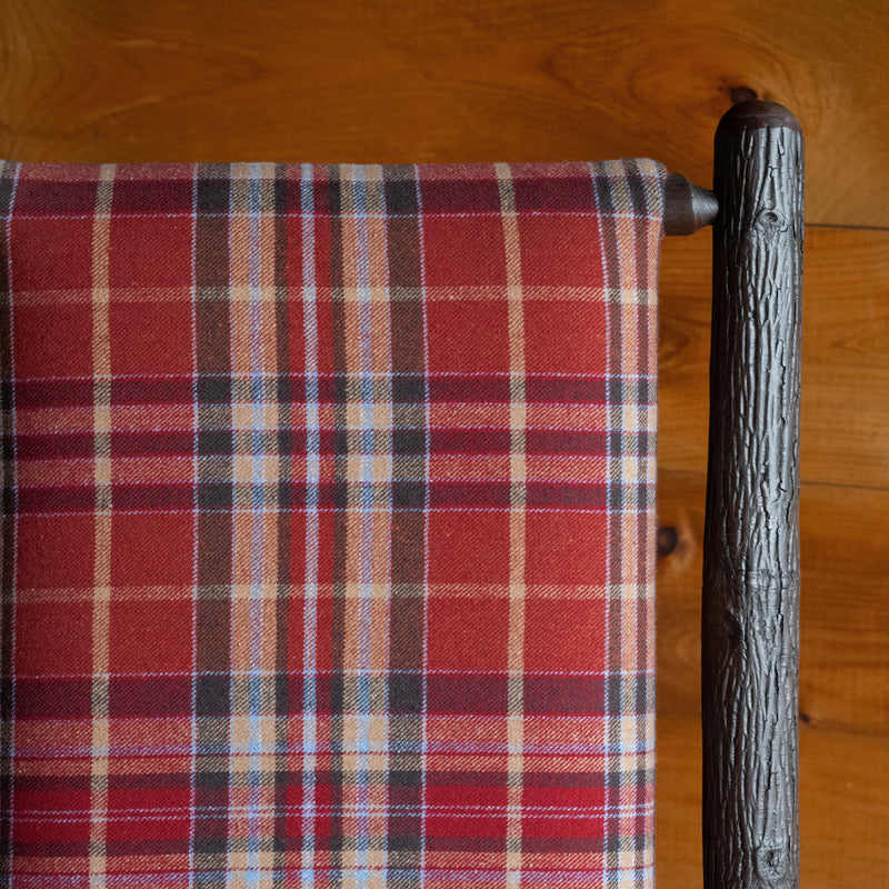 Close-up of the fabric of a chair upholstered in rustic red plaid against a rustic wooden wall