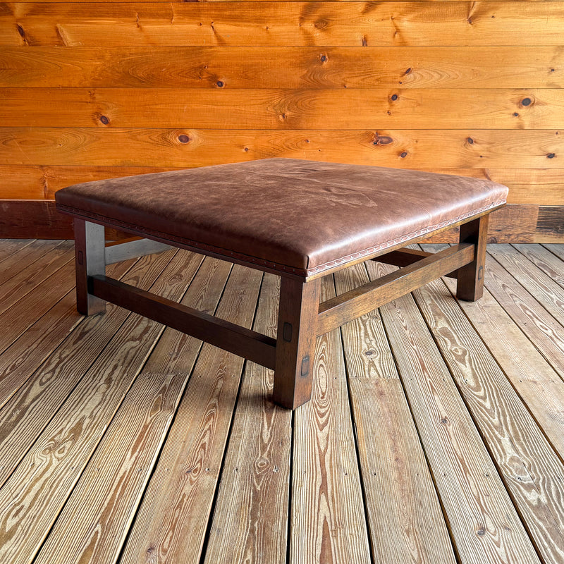 The angled view of a rustic leather ottoman with an open wooden frame against a wooden wall