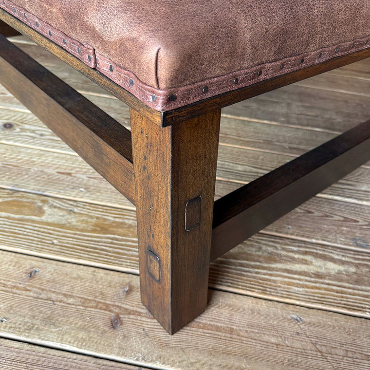 The angled view of a rustic leather ottoman with an open wooden frame against a wooden wall