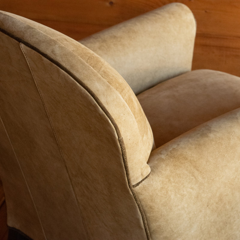 Close-up of the welt of a tight back leather arm chair upholstered in a rustic high-contrast leather against a rustic wooden wall