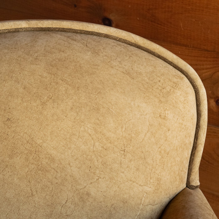 Close-up of the tight back of a leather arm chair upholstered in a rustic high-contrast leather against a rustic wooden wall
