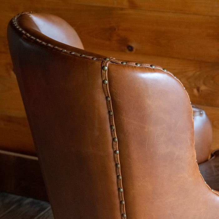 Close-up of the back of a brown leather wingback chair against a wooden wall