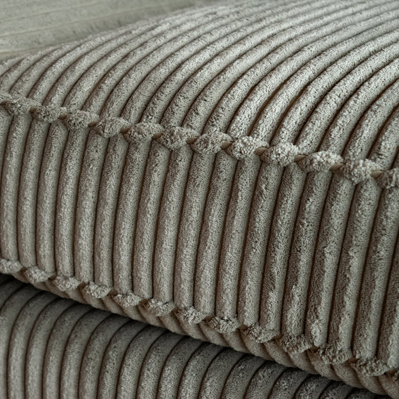Cushion welt detail of a three-seat sofa upholstered in a muted green corded velour fabric on a wooden floor against a wooden wall
