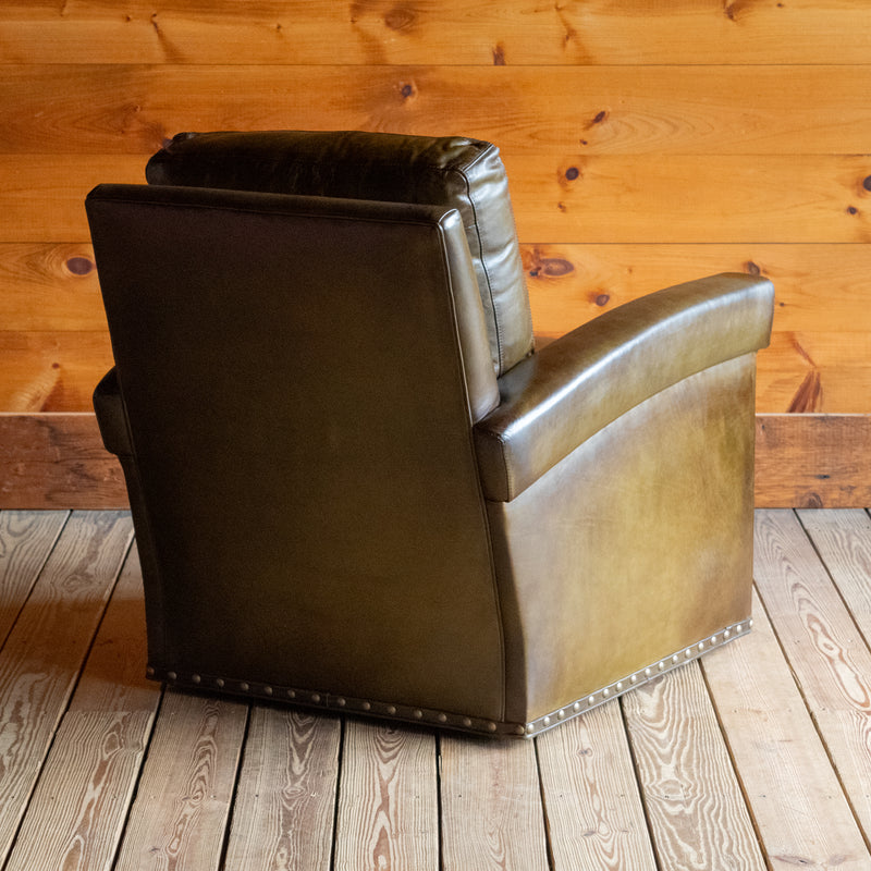 Angled back view of an olive green leather swivel chair against a wooden wall