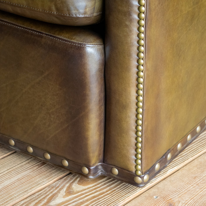 Close-up of the base of an olive green leather swivel chair against a wooden floor