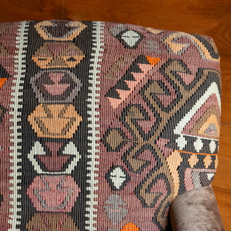 Close-up of the fabric of an armchair with brown, beige, and orange geometric patterned rug upholstery against a rustic wooden wall