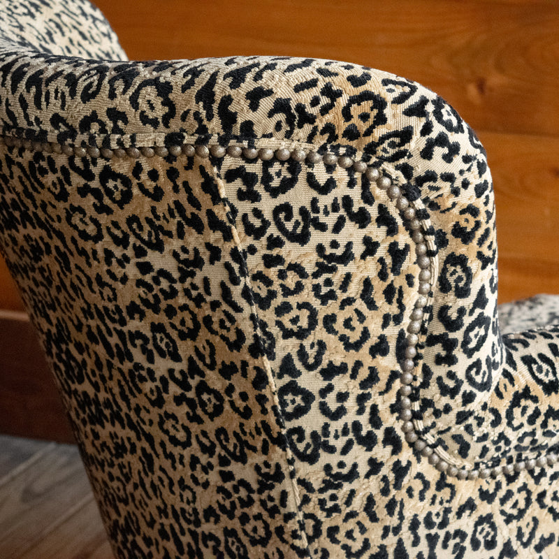 Close-up of the back corner of a petite arm chair upholstered in a jaguar print fabric against a wooden wall
