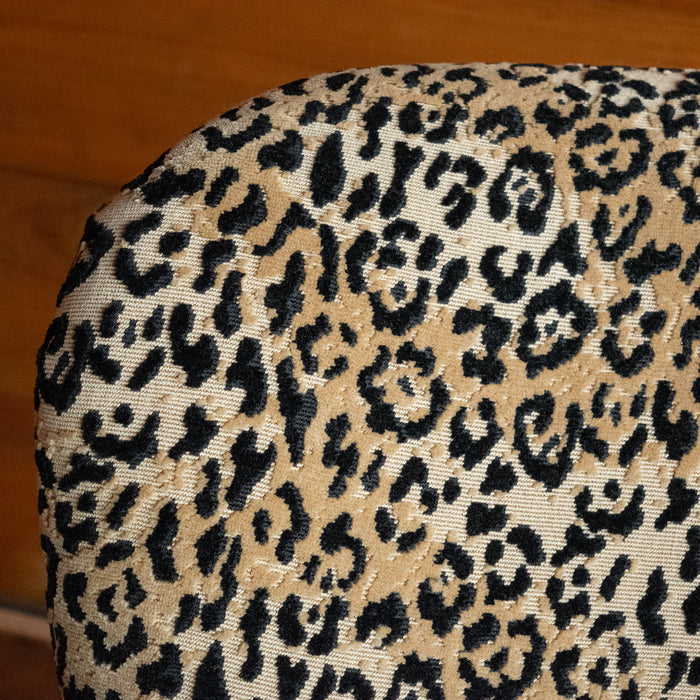Close-up of the seatback of a petite arm chair upholstered in a jaguar print fabric against a wooden wall