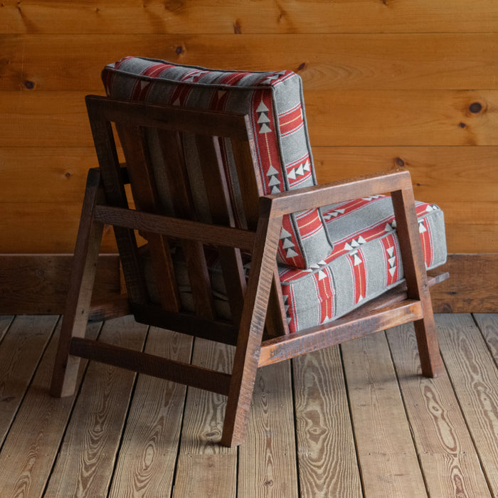 Angled back view rustic chair with light gray, red, and white geometric striped cushions on a reclaimed red oak frame, on a wide-plank wood floor against a rustic wooden wall