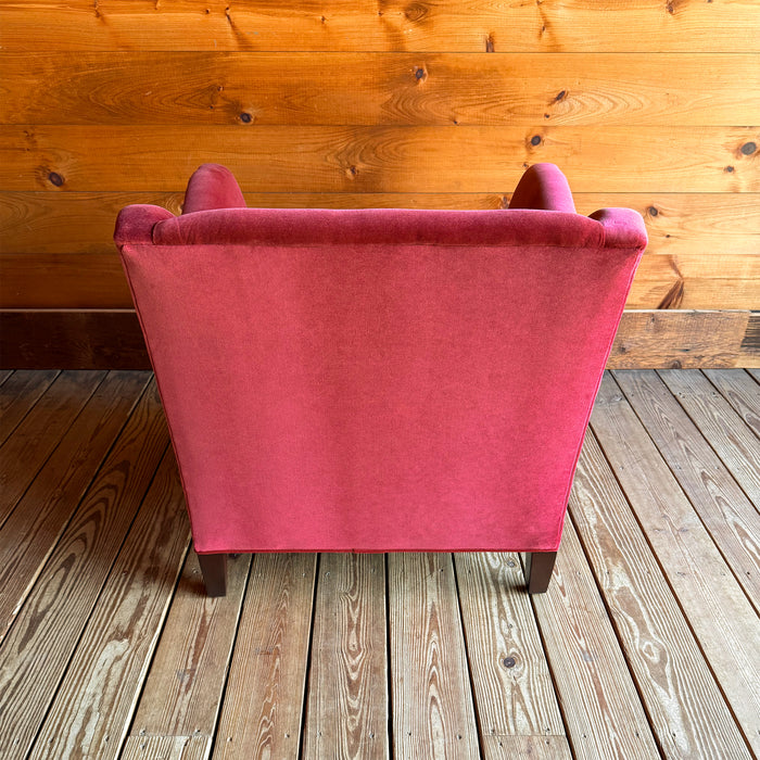 Back view of a red velvet armchair with a lumbar pillow against a wooden wall