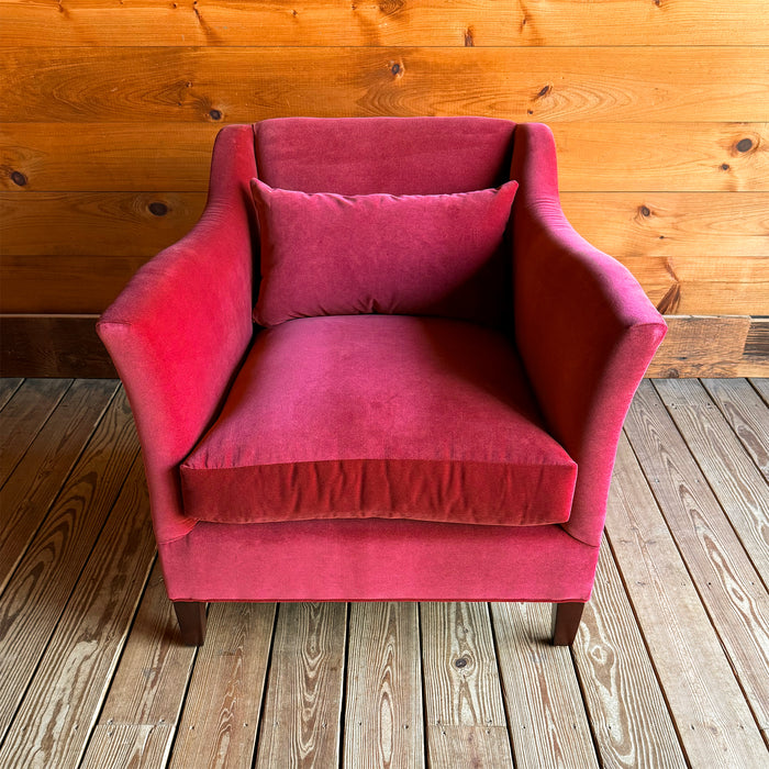 Front view of a red velvet armchair with a lumbar pillow against a wooden wall