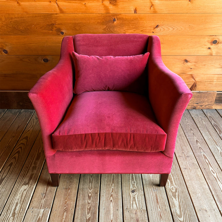 Back view of a red velvet armchair with a lumbar pillow against a wooden wall