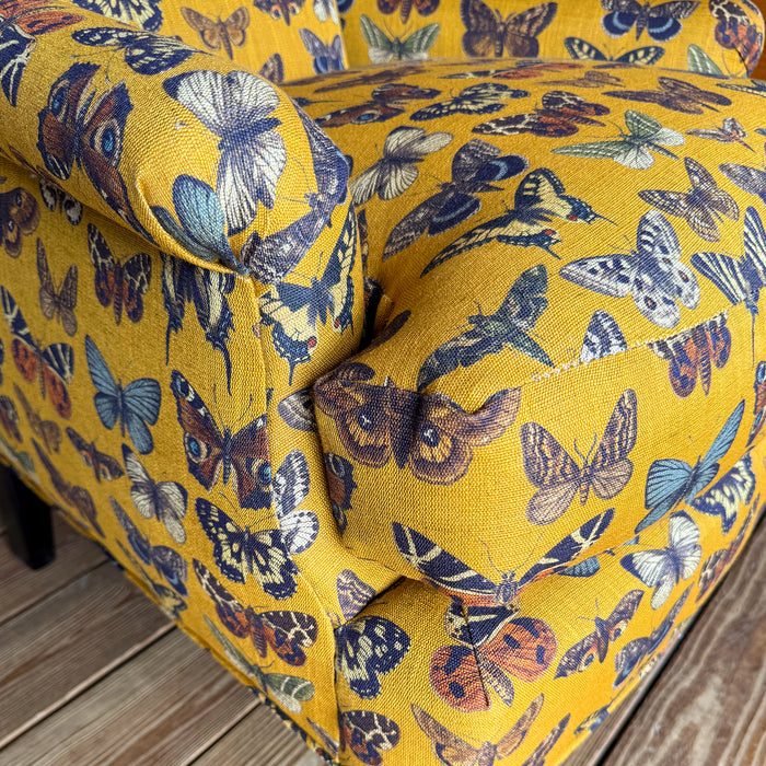 Arm and cushion close-up of an armchair upholstered in a yellow-gold fabric with an allover butterfly pattern