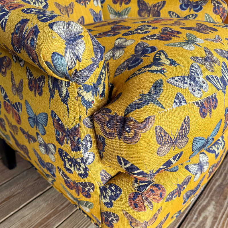 Arm and cushion close-up of an armchair upholstered in a yellow-gold fabric with an allover butterfly pattern