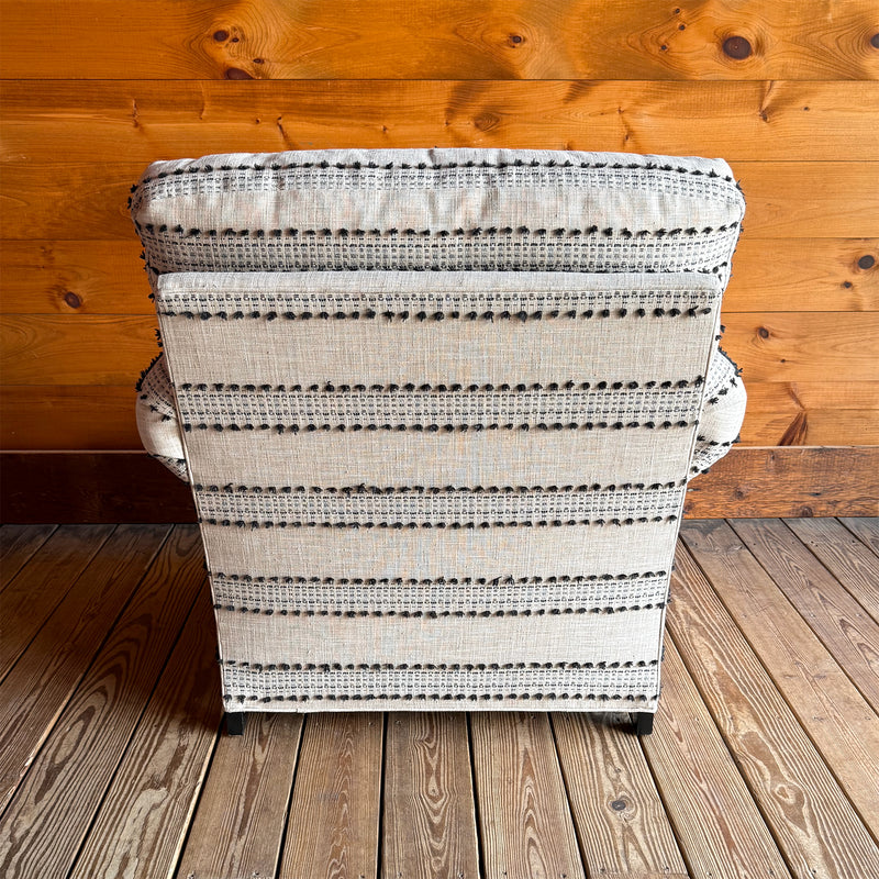 Back view of ivory and black striped roll arm chair with turned front legs against wooden wall.