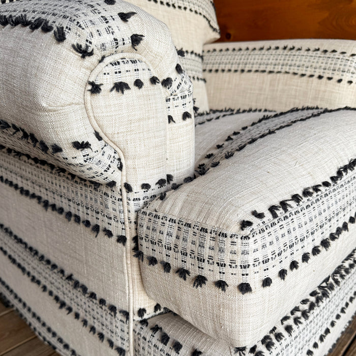 Close-up of the arm and cushion of a ivory and black striped roll arm chair.