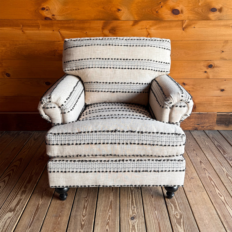 Front view of cream and black striped roll arm chair with turned front legs against wooden wall.