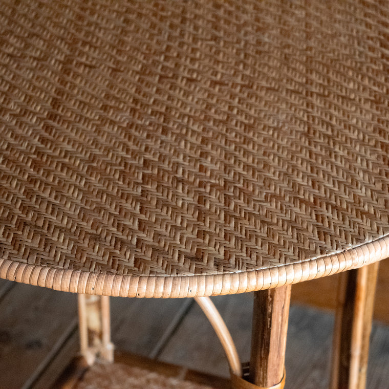 Front view of a bamboo side table with a round woven top against a wooden wall.