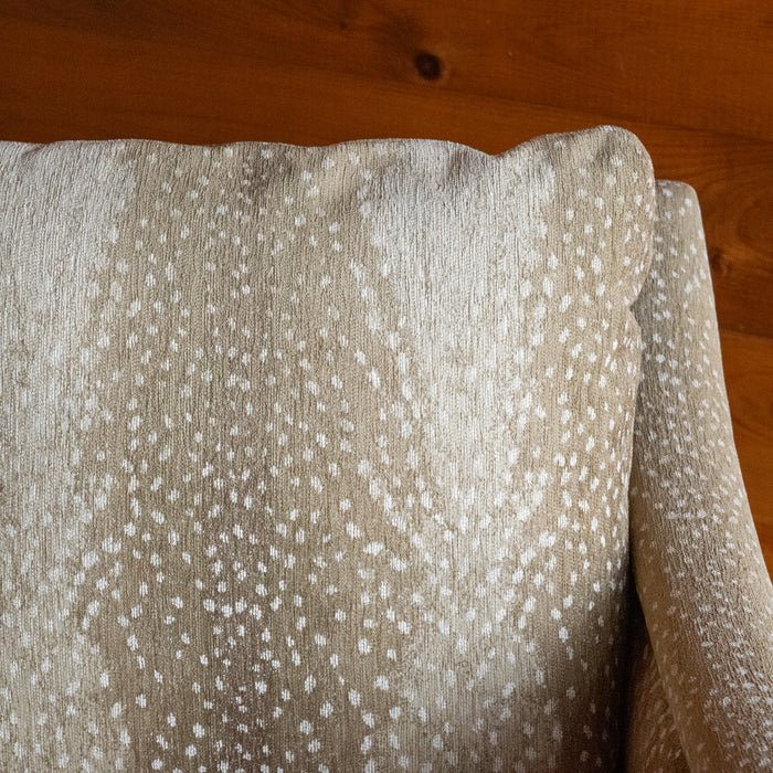 Close-up of the back cushion of a sloped arm chair upholstered in a spotted antelope-inspired fabric against a wooden wall