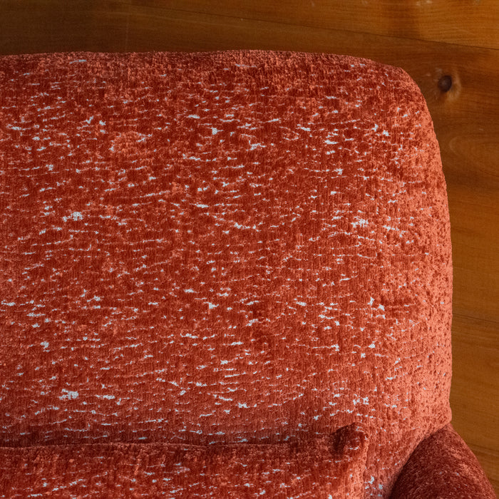 Close-up of the seat back a tomato-red armchair with a tight seat and back against a rustic wooden wall