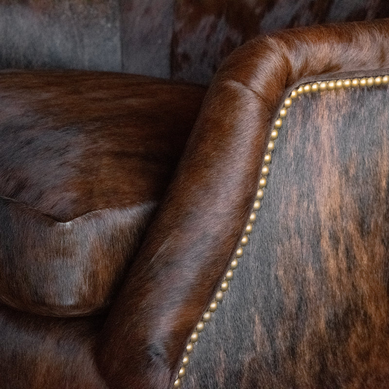 Closeup of the arm and seat cushion of a rustic arm chair upholstered in brindle hair-on-hide leather