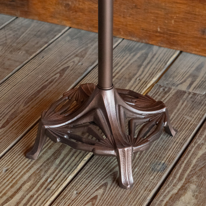 Close-up of the base of a rustic floor lamp with an oxidized bronze finish on a wide-plank wooden floor