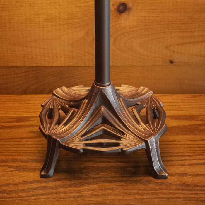 Close-up of the base of a rustic table lamp with an oxidized bronze finish on a wooden table against a rustic wooden wall