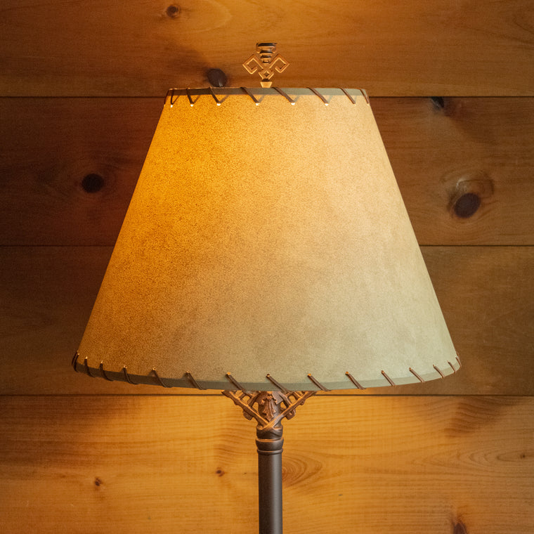 Close-up of the base of a rustic table lamp with an oxidized bronze finish on a wooden table against a rustic wooden wall