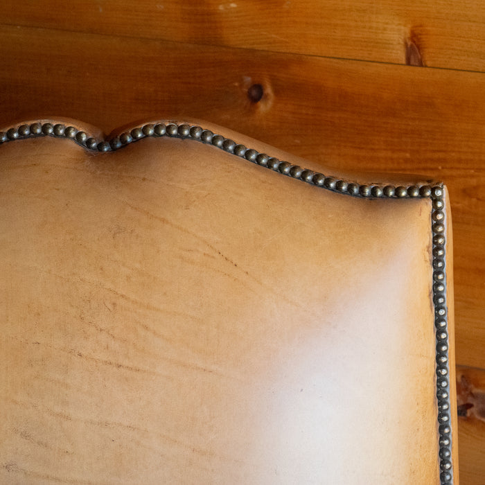 Close-up of the backrest of a rustic buffalo leather armchair against a wooden wall