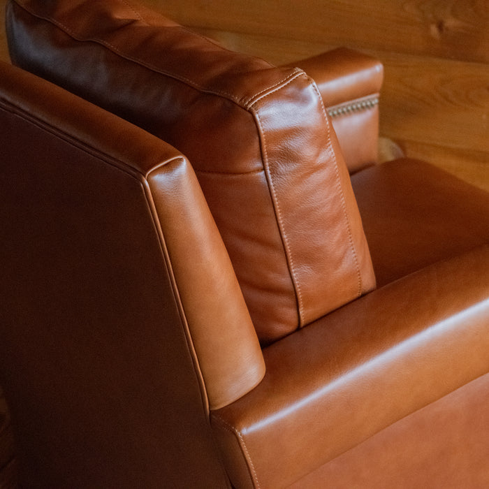 Close-up of the back corner of a rustic cognac leather swivel chair against a rustic wooden wall