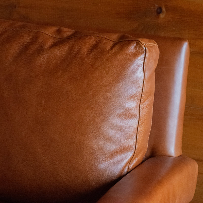Close-up of the back cushion of a rustic cognac leather swivel chair against a rustic wooden wall