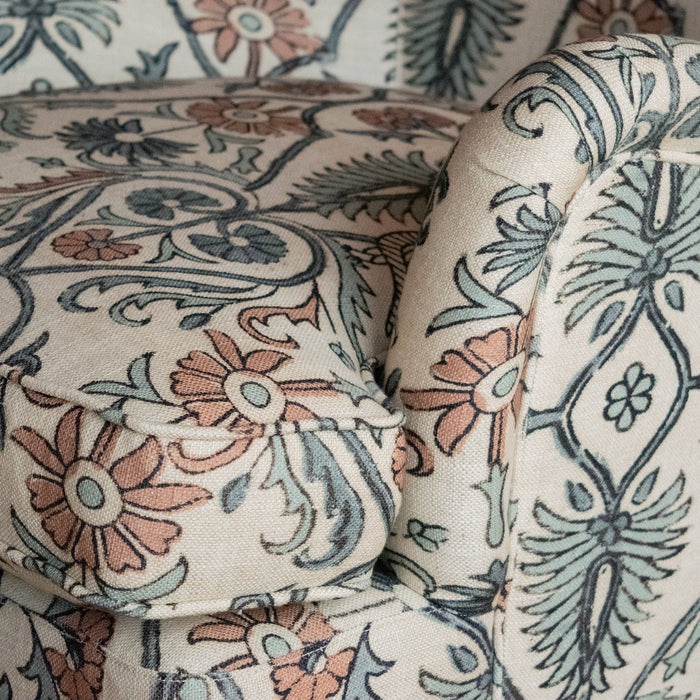 Close-up of the English rolled arm and seat cushion of an upholstered chair, highlighting the bird and botanical block print fabric and the fine welt trim detailing