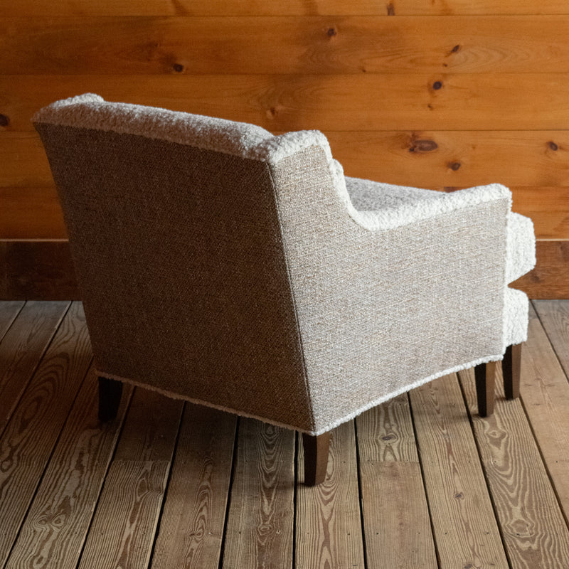 Angled back view of a tight back faux shearling chair on a wide-plank wooden floor against a rustic wooden wall