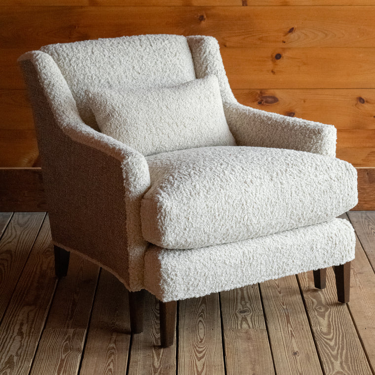 Angled back view of a tight back faux shearling chair on a wide-plank wooden floor against a rustic wooden wall