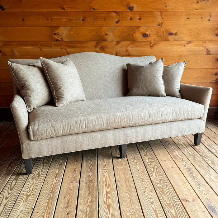 Angled front view of a bench seat cushion, tight back apartment sofa with flared arms, down throw pillows, and tapered legs on a wooden floor against a wooden wall